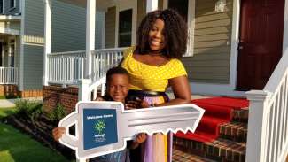 A mother and son holding large key cutout in front of their east college park home