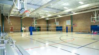 Wide shot of Optimist Park gym including volleyball net, bleachers and multiple basketball hoops. 