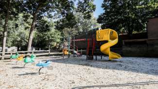 An outdoor playground with climbing equipment, a slide and sand surface