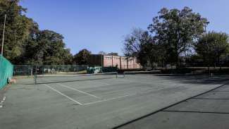 Two outdoor tennis courts with backboards and lighting 