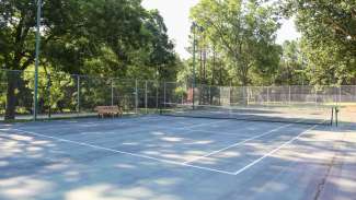 Two outdoor tennis courts with backboards and lighting 