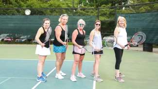 Group of adults posing for a picture on the tennis court 