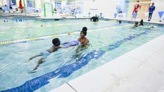 An instructor giving a little kid swim lessons and using a kick board 