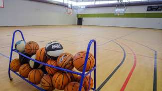 Indoor gymnasium with wooden floors and rack of basketballs