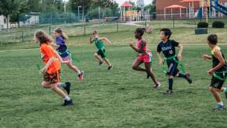 Kids running down green field playing flag football