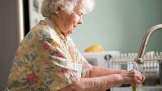 older woman washing vegetables under faucet