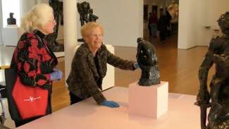 A visually impaired woman feeling a statue while wearing gloves at NCMA