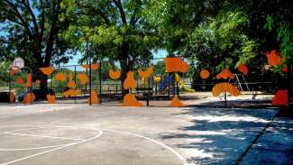 Public artwork of abstract orange shapes attached to a chain link fence by Jerstin Crosby