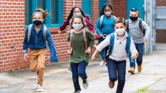 Kids in masks running outside school wearing backpacks