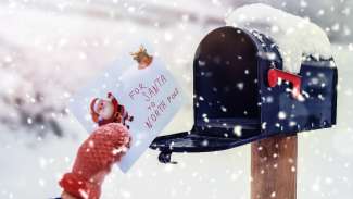 Hand wearing mittens putting letter to Santa in mailbox with snow 
