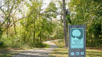 Sign for Capital Area Greenway with winding paved trail in background fading into trees