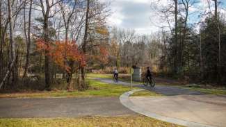 Sidewalk leading to the paved Neuse River greenway trail with two bicyclists