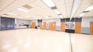 A large open dance studio type room with hardwood floors and a large mirorr.
