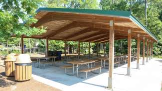 A outdoor picnic shelter with several tables and two nearby grills 