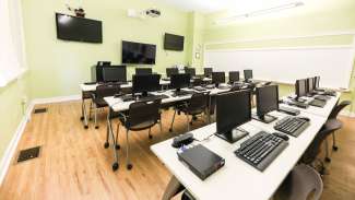 A technology room with desks, several computers and flat screen tv's 