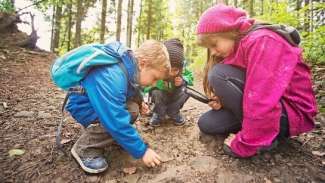 Three kids on muddy trail with magnifying glass looking at rock