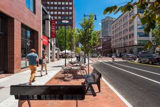 City street vie with people walking on the sidewalk with benches and outdoor seating