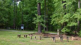 Wooden benches in grassy clearing surrounded by trees with fire put in middle
