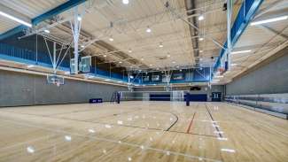 Inside of gymnasium with wood floors, bleachers, basketball goals, and second floor indoor track