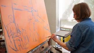 woman painting on a large orange canvas