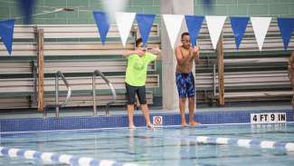 Two swimmers on deck, cheering unseen swimmers in pool
