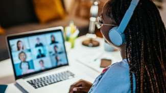 Woman with blue headphones looking at laptop with video chat