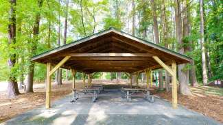 Picnic shelter with six picnic tables and trees in background