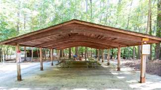 Picnic shelter with six picnic tables and trees in background