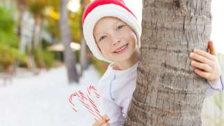 Smiling boy in Santa hat with an arm around a tree, holding candy canes