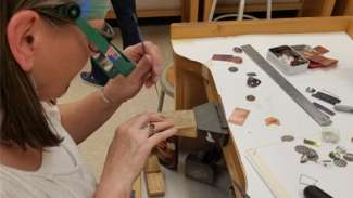 A teaching artist works with jewelry tools at a table filled with small metal pieces