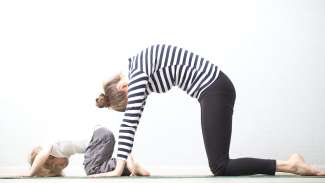 A mother and a child kneeling and bending forward with a rounded back, practicing yoga together.