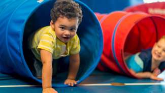 Two small children with smiles climbing out of a tunnel.