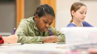 A girl sits at a table concentrating as she draws