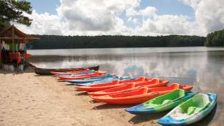Kayaks lined up on the beach of a lake right next to a boat house.