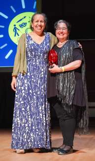 S.A. Corrin and Betty Siegel pose for the camera on stage while S.A. accepts an award