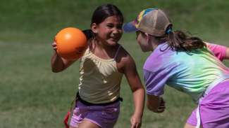 young girls playing with orange ball in field. 