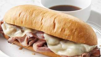 A french dip sandwich on a hoagie roll next to a bowl of beef consomme