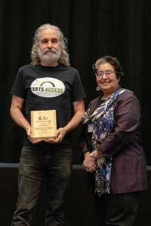 Dan Ellison holds a wood award plaque while standing next to Betty Siegel