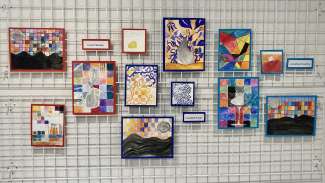 Student paintings hang on a grid wall at Pullen Arts Center