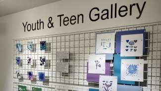 A metal grid on a wall decorated with prints made by youth and teens
