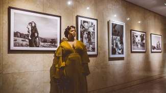 A woman in a yellow dress stands in front of photography by Phillip "King Phill" Loken