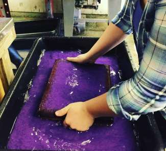 Papermaking artist with a screen filled with purple paper pulp. 