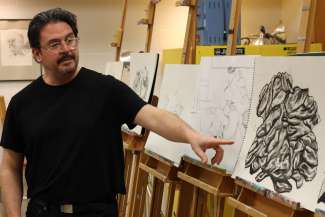 Artist Peter Marin demonstrating drawing and painting techniques pointing at an artwork on easel. 
