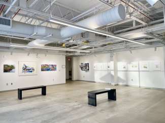 Gallery space with art displayed on walls and two benches in the center of the room.