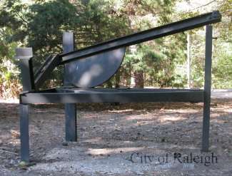Linear metal sculpture in a wooded area. 