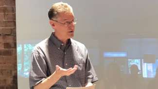 White man with short hair and glasses speaking in a classroom 