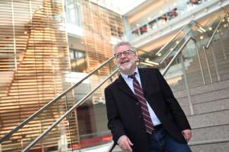 White man with a beard and dark rimmed glasses standing on a staircase, smiling. 