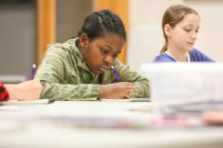Young Black teen working hard on a drawing at a table in an art studio. 