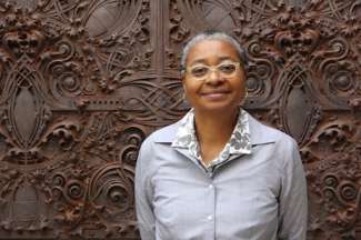 Artist Chandra Cox, a black women with short grey hair, clear-rimmed glasses and a grey oxford shirt. 