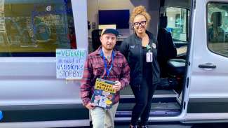 Officer Jackson (left) and VA worker Whitney Thomas (right) stand at the open door of the ban. Sign reads "Veteran? in need of assistance STOP BY!"